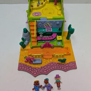 Può includere: Un playset Polly Pocket vintage dai colori vivaci, con un edificio a due piani con interni gialli ed esterni rosa e verdi. Include tre piccole statuette e formazioni di cactus e rocce.
