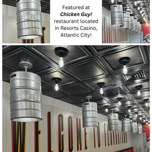 May include: A series of industrial-style pendant lights, shaped like beer kegs, hang from a black ceiling. The lights are silver with a white interior, illuminating the space below. The wall features the word "WELCOME" in large letters.