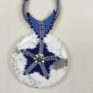 May include: A beaded necklace with a large, round, white stone pendant with grey veining. A beaded star in navy and silver decorates the pendant, with a silver flower centre. The necklace has a silver and navy beaded chain.