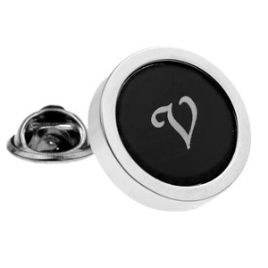 Peut inclure: Une épingle argentée avec un bouton circulaire noir orné d'une lettre "V" stylisée blanche.
