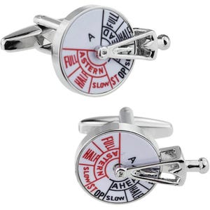 May include: A pair of silver cufflinks with a white dial and red lettering. The dial features a ship's wheel with a lever and the words "Full Astern", "Half Astern", "Slow", "Stop", "Slow", "Half Ahead", "Full Ahead".