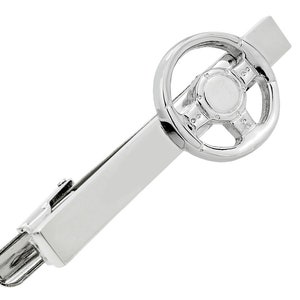 May include: A silver-colored tie clip featuring a detailed steering wheel design. The clip has a rectangular bar with a clasp, and the steering wheel is the focal point, adding a touch of automotive flair to formal wear.