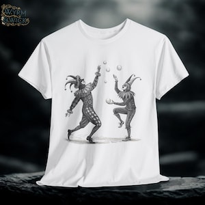 May include: White t-shirt featuring a black and white illustration of two jesters juggling balls. The jesters are dressed in traditional attire with hats and ruffled collars. The shirt has a classic crew neck.