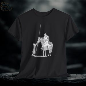 May include: Black t-shirt with a grayscale illustration of a knight on horseback, reaching towards a child. The design includes a spear and a medieval theme. The shirt has a crew neck and short sleeves.