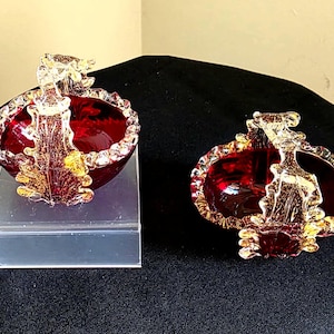 May include: Two decorative glass baskets with a deep red interior and gold-coloured accents. The baskets have a handle and a decorative rim. One basket is on a clear stand.