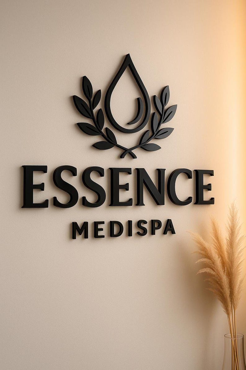 May include: Black 3D sign on a beige wall. The sign features the word "ESSENCE" above "MEDISPA". A black water droplet design with leaves is above the text. A vase of dried plants is in the lower right corner.