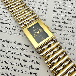 May include: A vintage gold-toned wristwatch with a rectangular black face. The watch features a gold band with silver accents and Roman numeral hour markers. The watch face displays the brand name "Piera Nicol" and the word "QUARTZ".