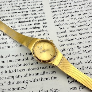 May include: A white ceramic mug with a black handle and the text "But First, Coffee" in a bold, black font. The mug is set against a blurred background, suggesting a cozy setting. The mug appears to be approximately 4 inches tall.