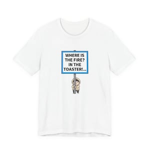 Puede incluir: Camiseta blanca con un dibujo de una persona sosteniendo un letrero azul con texto blanco: "WHERE IS THE FIRE? IN THE TOASTER!..." La persona lleva una chaqueta con capucha. Prenda de vestir informal.