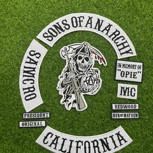 Op de afbeelding: Een verzameling geborduurde patches met het thema Sons of Anarchy. De patches tonen een zeisdrager met een geweer, de woorden "Sons of Anarchy", "California", "Samcro" en andere zinnen in wit op een zwarte achtergrond.