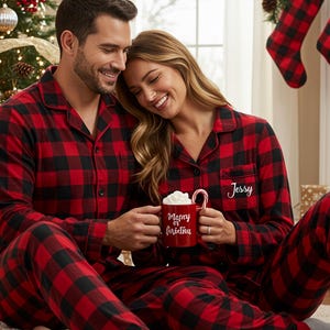 May include: Matching red and black plaid pajama sets. A person holds a red mug with whipped cream and a candy cane. The mug says "Merry or Christmas". The pajama top has the name "Jessy" embroidered on it.