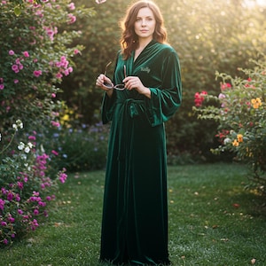 May include: A long, emerald green velvet robe with a matching belt. The robe has wide sleeves and is personalized with the name "Kelly" embroidered on the chest. The image is set outdoors with a garden background.