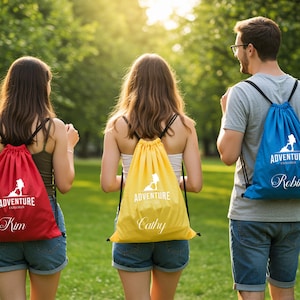 May include: Three drawstring backpacks in red, yellow, and blue are worn by people walking in a park. Each bag has the words "Adventure Explorer" and a silhouette graphic. The red bag says "Kim", the yellow bag says "Cathy", and the blue bag says "Robin".