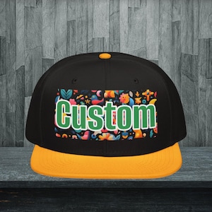 Könnte beinhalten: Schwarze und gelbe Baseballkappe mit flachem Schirm und dem Wort "Custom" in Grün und Weiß. Die Kappe hat ein farbenfrohes Blumen- und Vogelmuster auf der Vorderseite.