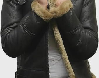 May include: Black leather jacket with a shearling collar and trim. The jacket features a zip-up front, a buckled belt, and a classic aviator style. The shearling is a light brown color, and the jacket appears to be well-made and durable.