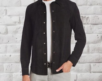 Peut inclure: Chemise noire à manches longues avec col classique. La chemise présente un motif texturé et est portée sur un t-shirt blanc. La chemise est associée à un pantalon gris et une ceinture noire. Le fond est un mur de briques blanches.