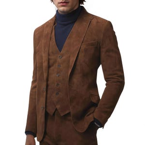 May include: A three-piece brown suede suit with a matching blazer, vest, and trousers. The blazer has a notched lapel and two-button closure. The vest has a button-down front. The suit is paired with a navy blue turtleneck.