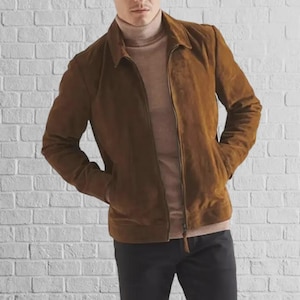 May include: A brown suede jacket with a collared neckline and a zipper closure. The jacket has two front pockets and is worn over a light brown turtleneck. The person is wearing black pants.
