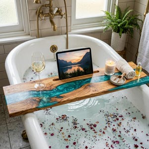 Könnte beinhalten: Ein hölzernes Badewannen-Tablett mit einem tealfarbenen Harzfluss-Design, das ein Tablet, eine Kerze und anderes Badzubehör hält. Ein Glas Weißwein steht in der Nähe. Das Tablett überspannt die Breite einer weißen Badewanne mit Wasser und Rosenblättern.