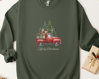 May include: An olive green sweatshirt featuring a watercolor design of a red vintage truck carrying gifts and Christmas trees. The words "Merry Christmas" are written below the truck in a script font.