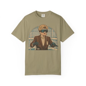 May include: Khaki t-shirt with a vintage illustration of a woman wearing futuristic glasses and gloves. She is dressed in a brown blazer and a pearl necklace. The year "1993" is printed below the image. The design has a retro, comic book style.