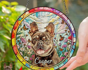 May include: A round, stained-glass window hanging with a French Bulldog portrait. The dog is brown and tan, surrounded by flowers, butterflies, and the name "Cooper". The border is a colorful mosaic, and the background is a sky scene.