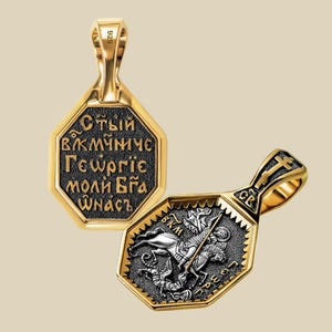 May include: Two gold-toned pendants with octagonal frames. One pendant features Cyrillic text on a black background. The other pendant depicts a knight on horseback slaying a dragon. The pendants have a textured border and a loop for a chain.