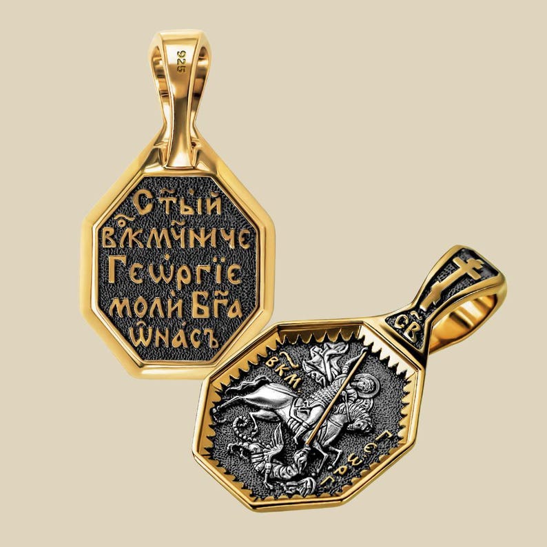 May include: Two gold-toned pendants with octagonal frames. One pendant features Cyrillic text on a black background. The other pendant depicts a knight on horseback slaying a dragon. The pendants have a textured border and a loop for a chain.