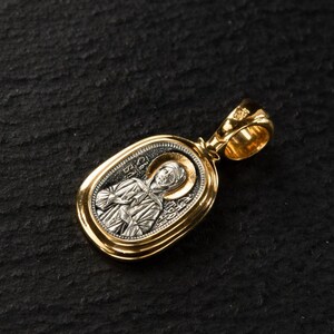 May include: Gold pendant with an oval, silver-coloured centre depicting a religious figure with a gold halo. The pendant has a detailed design and a loop for a chain.