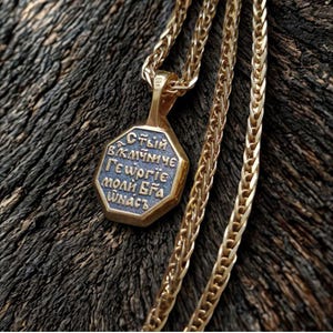 May include: A gold-colored pendant necklace with an octagonal charm. The charm has blue text and a gold border. The chain is a wheat chain style. The necklace is displayed on a dark wood surface.