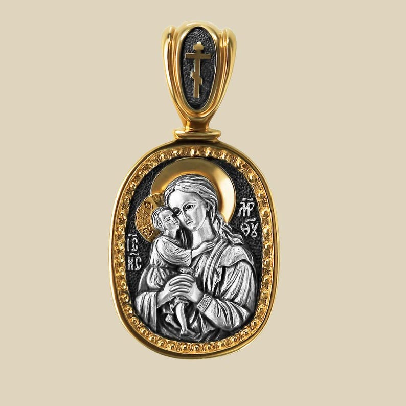 May include: An oval pendant in gold and silver, depicting a religious icon of a woman and child. The pendant has a gold border and bail, with a cross at the top. The icon is detailed with religious text.