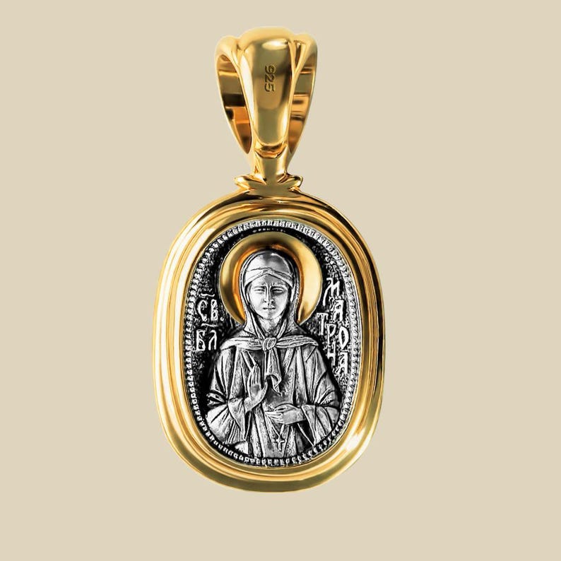 May include: A gold-plated pendant with a religious icon. The oval pendant has a detailed silver image of a saint with a halo, set in a gold frame. The bail is gold, stamped with "925". The pendant is likely made of silver.
