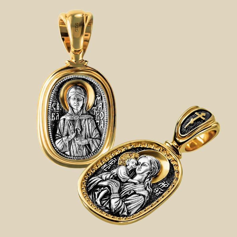 May include: Two gold-coloured pendants with religious iconography. One pendant features a woman with text, the other depicts a woman holding a child. Both pendants have a gold frame and a silver-coloured centre.
