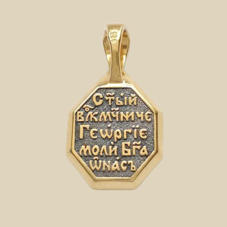 May include: Gold-toned pendant with an octagonal face and a loop for a chain. The pendant features Cyrillic text in a contrasting dark color, framed by a gold border. The pendant is likely made of gold.