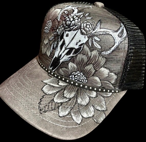 Hand-Burned gray trucker hat, black mesh snap back. Floral w/deer skull. Silver & white acrylic paint accents. Can add personalized wording.