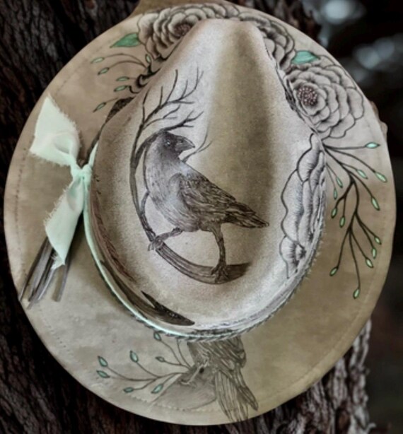 Crow fedora hat, hand burned with a wood burning tool. Painted metallic pale pink feathers, teal green foliage, grey vegan suede.