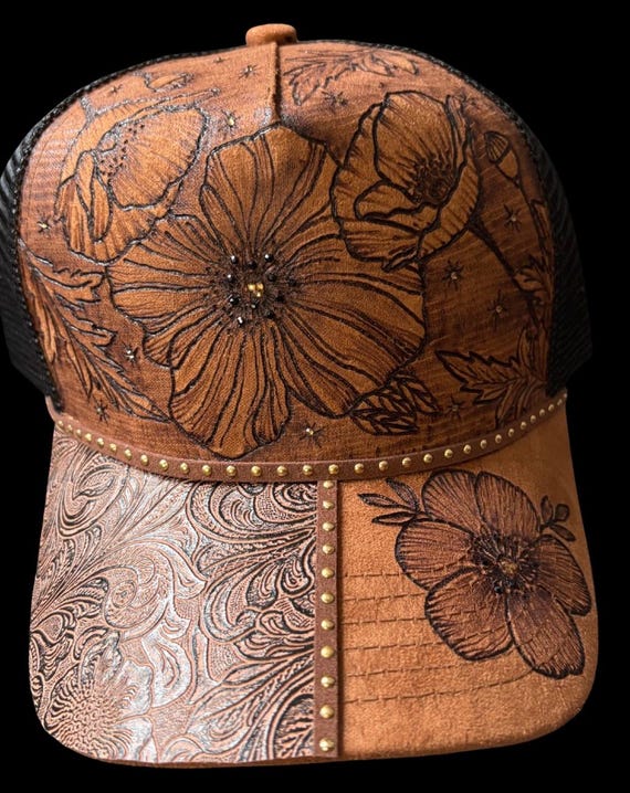Hand-Burned caramel color trucker hat, black mesh snap back. Gorgeous floral w/bronze rhinestones. Can add personalized wording.