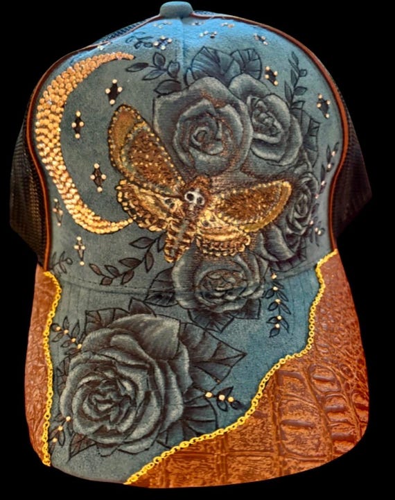Death’s Head Hawk Moth, hand-burned, teal faux suede with black mesh ponytail back. Moth is hand painted, rhinestones, brown faux leather