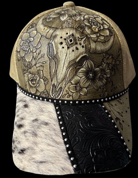 Steer skull hand-burned Vegan (faux) suede ponytail ball cap. Faux fur hide & tooled faux leather on brim. Rhinestones, mesh ponytail back.
