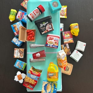 May include: A collection of miniature food items, including a carton of Breyers ice cream, a bottle of Sunny D, and a bag of Ore-Ida Golden Crinkles, arranged around a small, turquoise refrigerator. Other items include popcorn, snacks, and condiments.