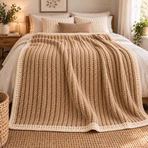 May include: A rectangular crochet blanket featuring a textured vertical ribbed pattern in a light tan color. The blanket is finished with a solid cream-colored border that frames the entire piece, creating a distinct contrast against the tan center.