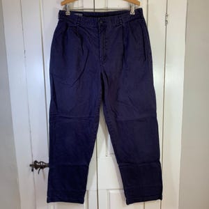 May include: A pair of dark navy blue trousers featuring a pleated front, a button and zipper fly closure, belt loops, and side pockets. The pants have a straight-leg cut and are constructed from a solid-colored fabric with a visible waistband.