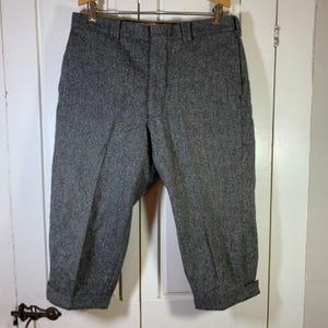 May include: A pair of charcoal gray trousers featuring a textured, speckled wool-like fabric. These pants include a structured waistband with belt loops, a front zipper fly, and straight-cut legs that end in a clean, folded cuff at the bottom hem.