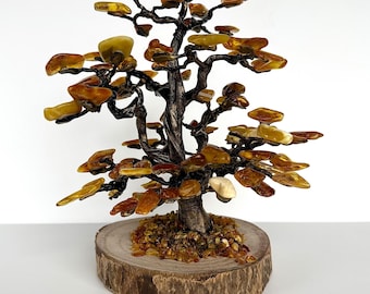 May include: A decorative amber tree sculpture. The tree features a dark brown trunk and branches with amber-colored leaves. It is set on a round wooden base with amber chips. The sculpture is a unique home decor item.