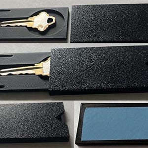 May include: A black key holder with a textured surface, featuring a gold and silver key. The holder has a sliding cover and a slot for the key. The key holder is shown open and closed.