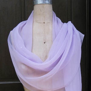 May include: A lavender sheer shawl with a delicate drape. The shawl is made of a lightweight fabric and has a soft, flowing texture.