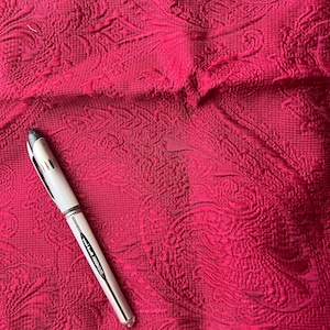May include: A silver pen with black ink on a red fabric background with a paisley pattern.