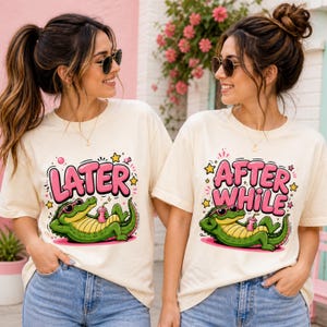 May include: Two women wearing cream-colored t-shirts with a cartoon alligator design. One shirt says "LATER" and the other says "AFTER WHILE" in pink bubble letters. The alligator is green, wearing sunglasses, and holding a drink.