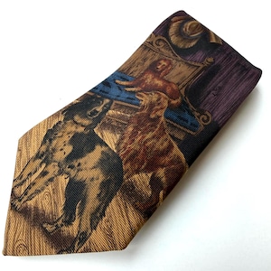 May include: A necktie featuring a printed scene of two dogs on a wooden floor, with one dog in black and brown and the other in shades of brown. The background includes a blue chair, a purple curtain, and a brown hat, all on a textured fabric.