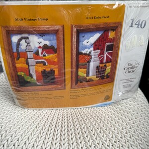 May include: A needlepoint kit package titled The Creative Circle featuring two designs, 0140 Vintage Pump and 0141 Dairy Fresh. Each design shows a rural landscape with a barn, fields, and a bucket, with a finished size of 5 inches by 7 inches.